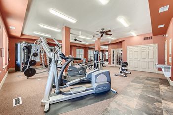 A spacious gym with a variety of equipment including treadmills, weights, and a bench press at Fox Run Lofts Apartments, Englewood CO.